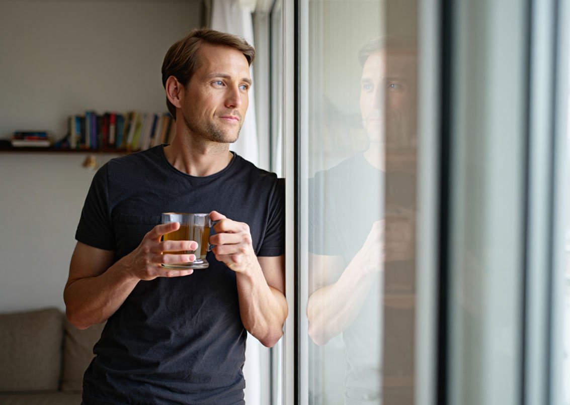 Мужчина пьет чай и смотрит в окно
